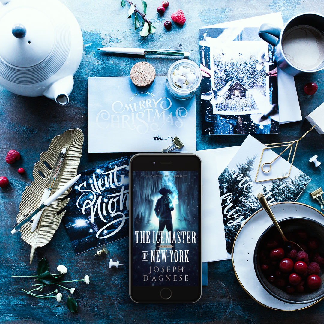 The Icemaster of New-York book cover by Joseph D'Agnese, featuring a mysterious man in 17th-century Dutch attire standing in a shadowy cavern with hanging icicles. Image appears on a smart phone amid a decorative winter tabletop scene, set against a blue and white backdrop, symbolizing a dark fantasy prequel about an immortal Jack Frost. 
