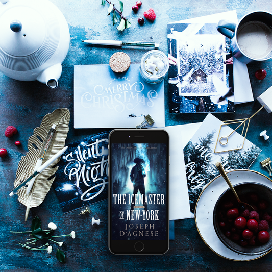 The Icemaster of New-York book cover by Joseph D'Agnese, featuring a mysterious man in 17th-century Dutch attire standing in a shadowy cavern with hanging icicles. Image appears on a smart phone amid a decorative winter tabletop scene, set against a blue and white backdrop, symbolizing a dark fantasy prequel about an immortal Jack Frost. 