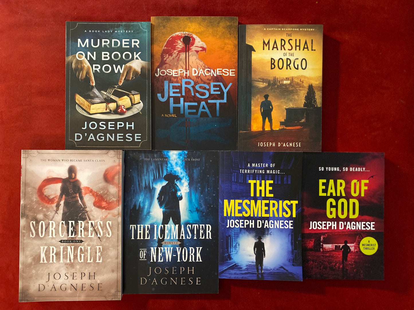 Joe's Paperback Writer Bundle book cover by Joseph D'Agnese, featuring a real-life photo of seven paperback books fanned out, including titles like Jersey Heat, The Marshal of the Borgo, and Sorceress Kringle. The image represents a massive multi-genre collection of 2,200 pages of thriller, mystery, and fantasy novels.