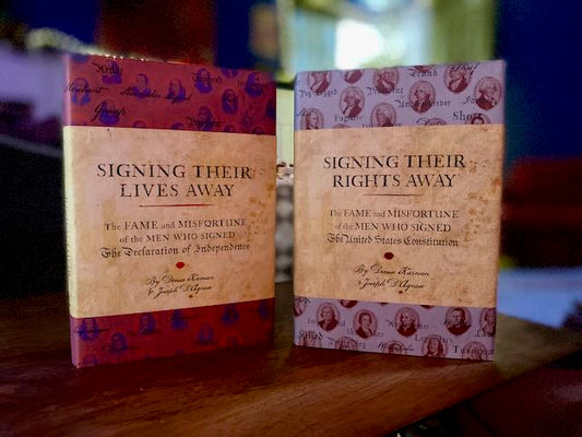 Signing Their Lives Away and Signing Their Rights Away hardcover books standing upright on a desk, displaying their dust jackets with thumbnail portraits of the signers. Two autographed editions by Joseph D'Agnese and Denise Kiernan.