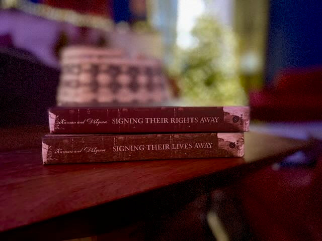 Signing Their Lives Away and Signing Their Rights Away hardcover books without dust jackets, revealing their faux distressed old-timey hardcover spines and bindings. The vintage-style covers replicate the look of 18th-century leather-bound volumes.