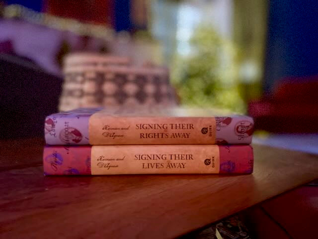 The two autographed hardcovers of Signing Their Lives Away and Signing Their Rights Away stacked on top of each other with dust jackets on, showing the spine text and thumbnail portrait design. Pristine collector's condition.